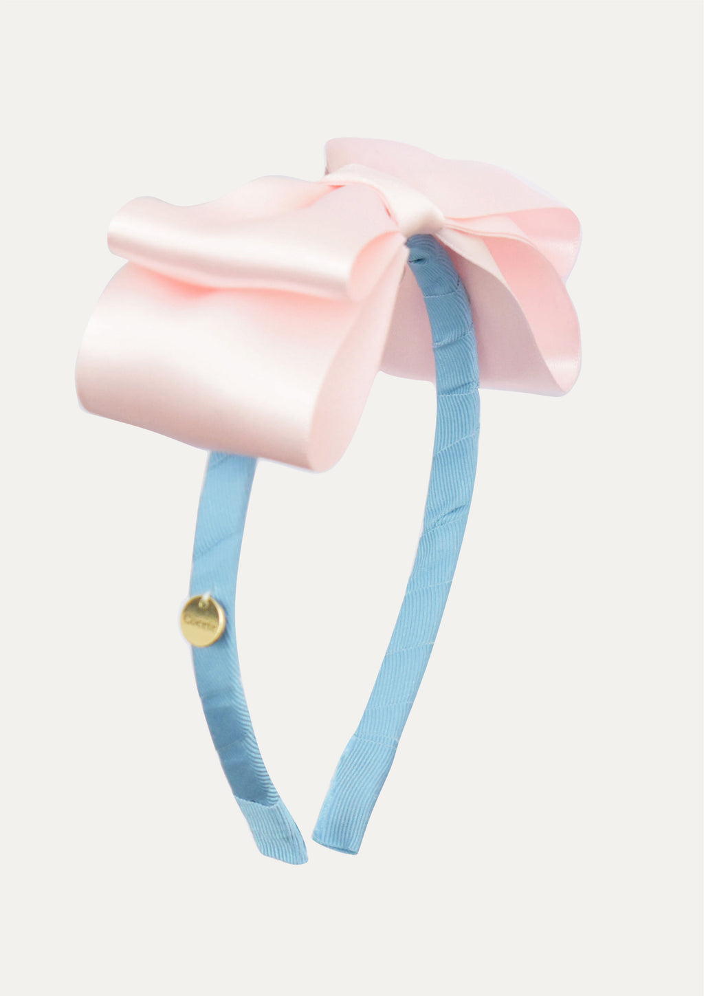 Handmade large light pink satin bow headband for girls, featuring a blue ribbon-covered band and a small gold COCETE brand charm.