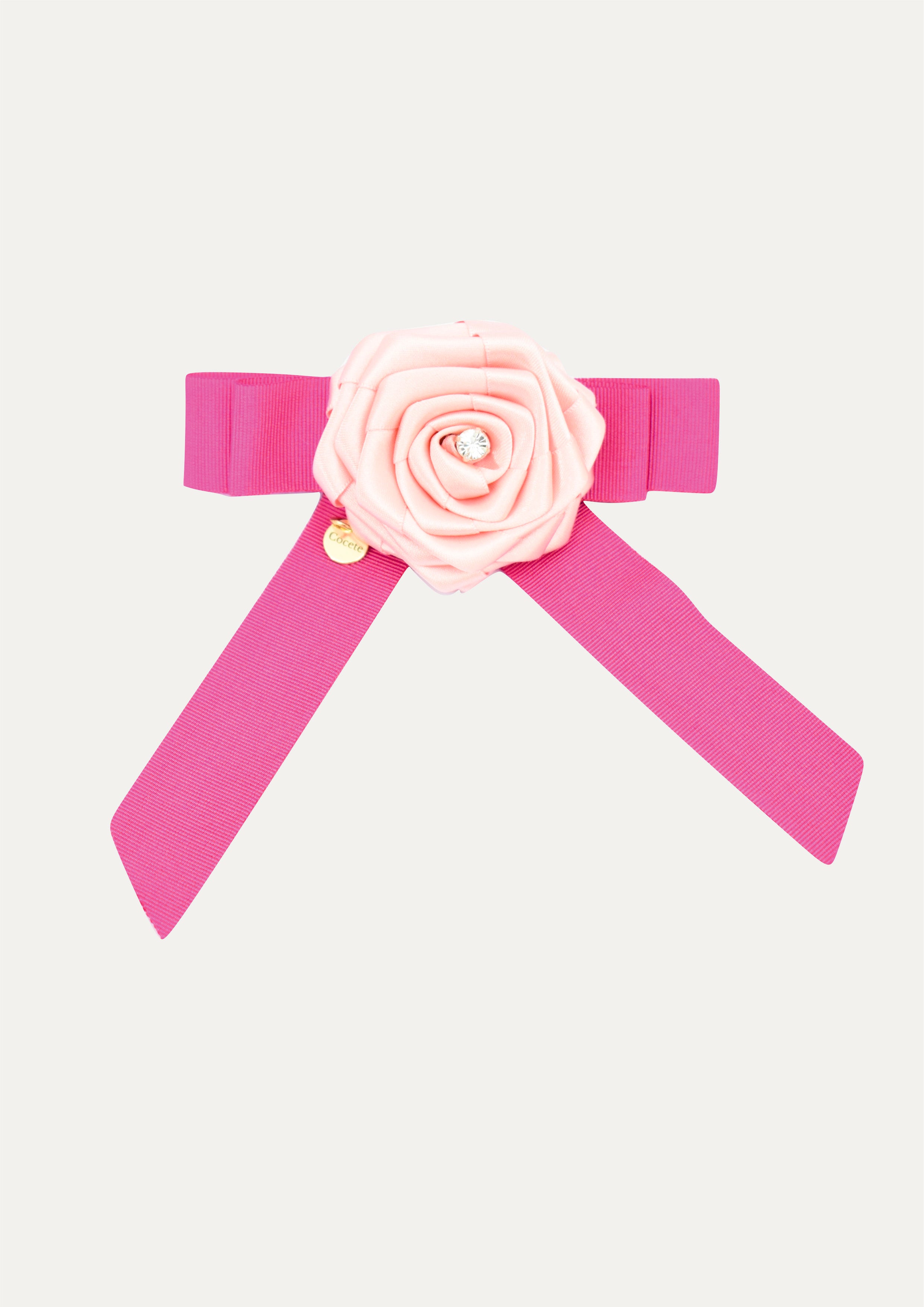 Handmade fuchsia pink ribbon hair bow for girls, decorated with a pale pink satin rose, a crystal center, and a gold COCETE brand charm.