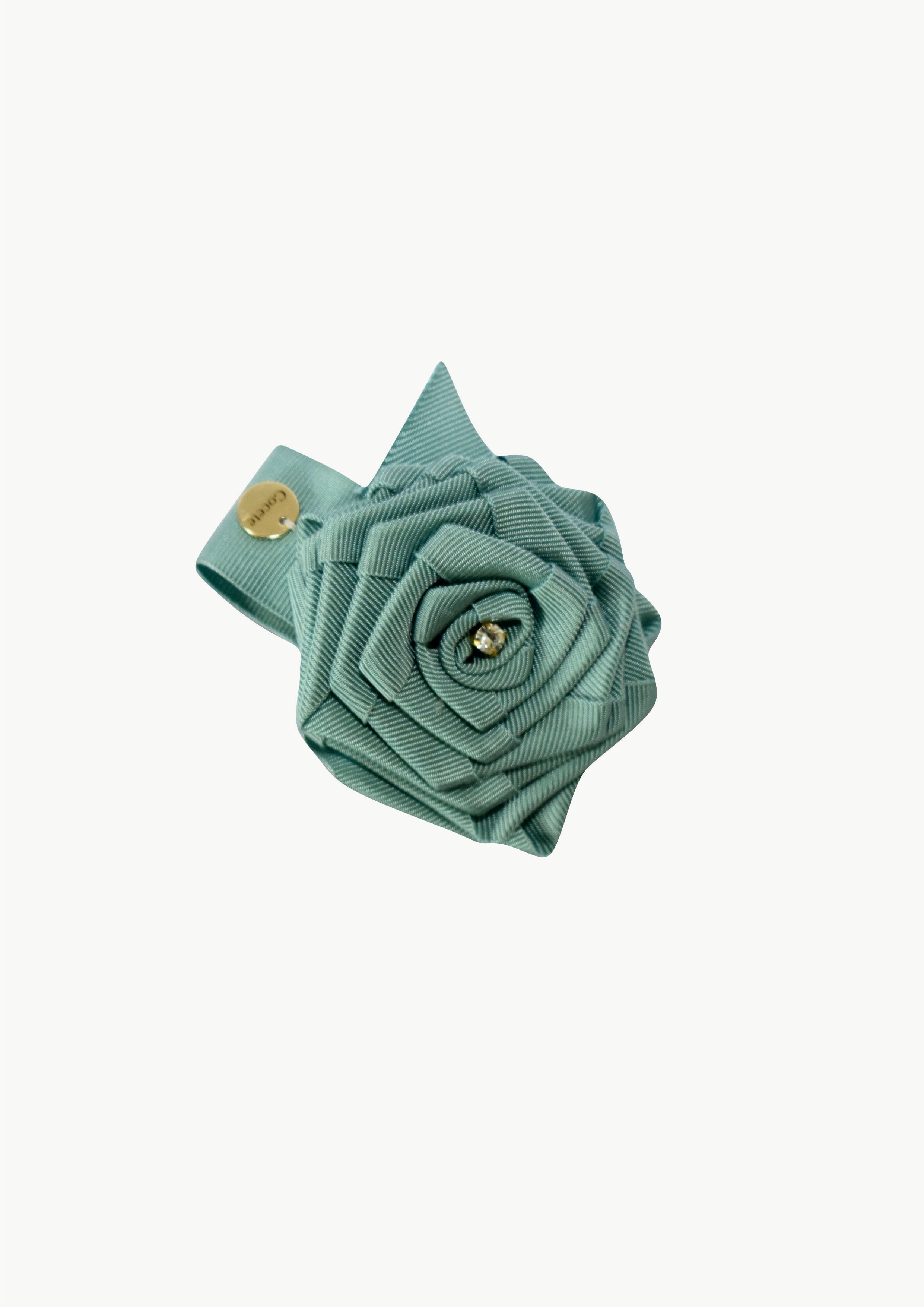 Handmade sage green fabric rose hair clip for girls with a sparkling crystal center and a gold COCETE brand charm.