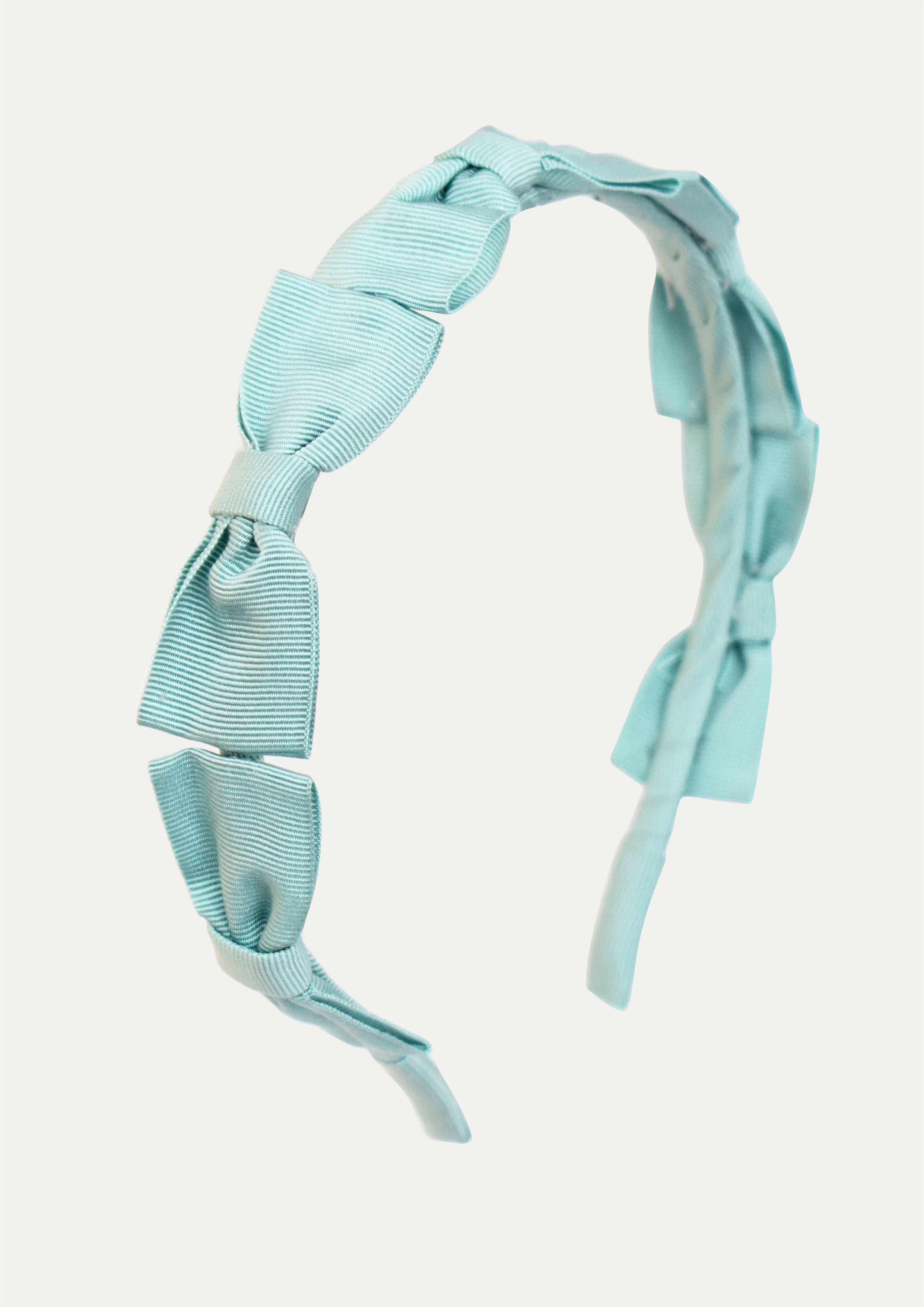 Handmade mint green headband for girls featuring a series of small grosgrain ribbon bows, isolated on a white background.
